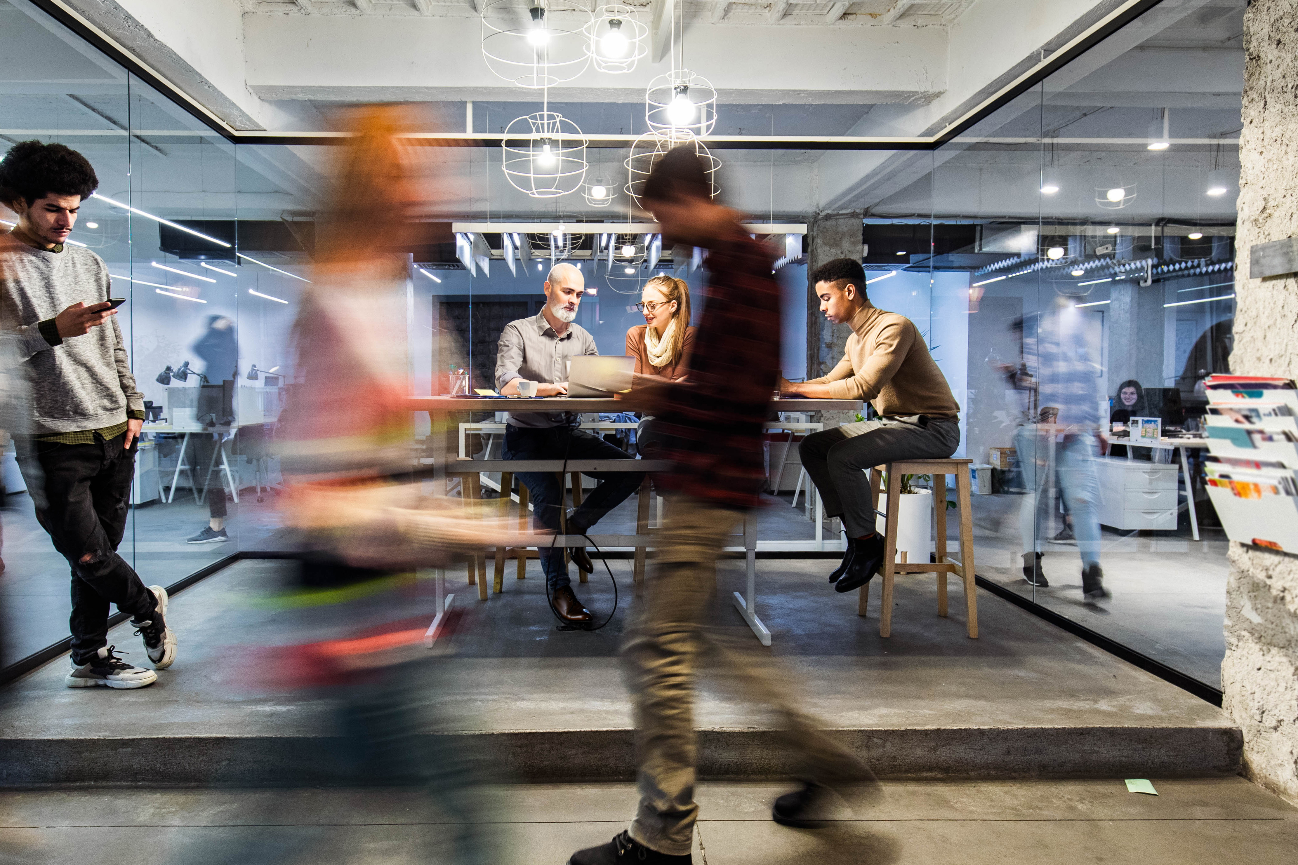 Group of young freelancers working on wireless technology at casual office. Some people are in blurred motion.