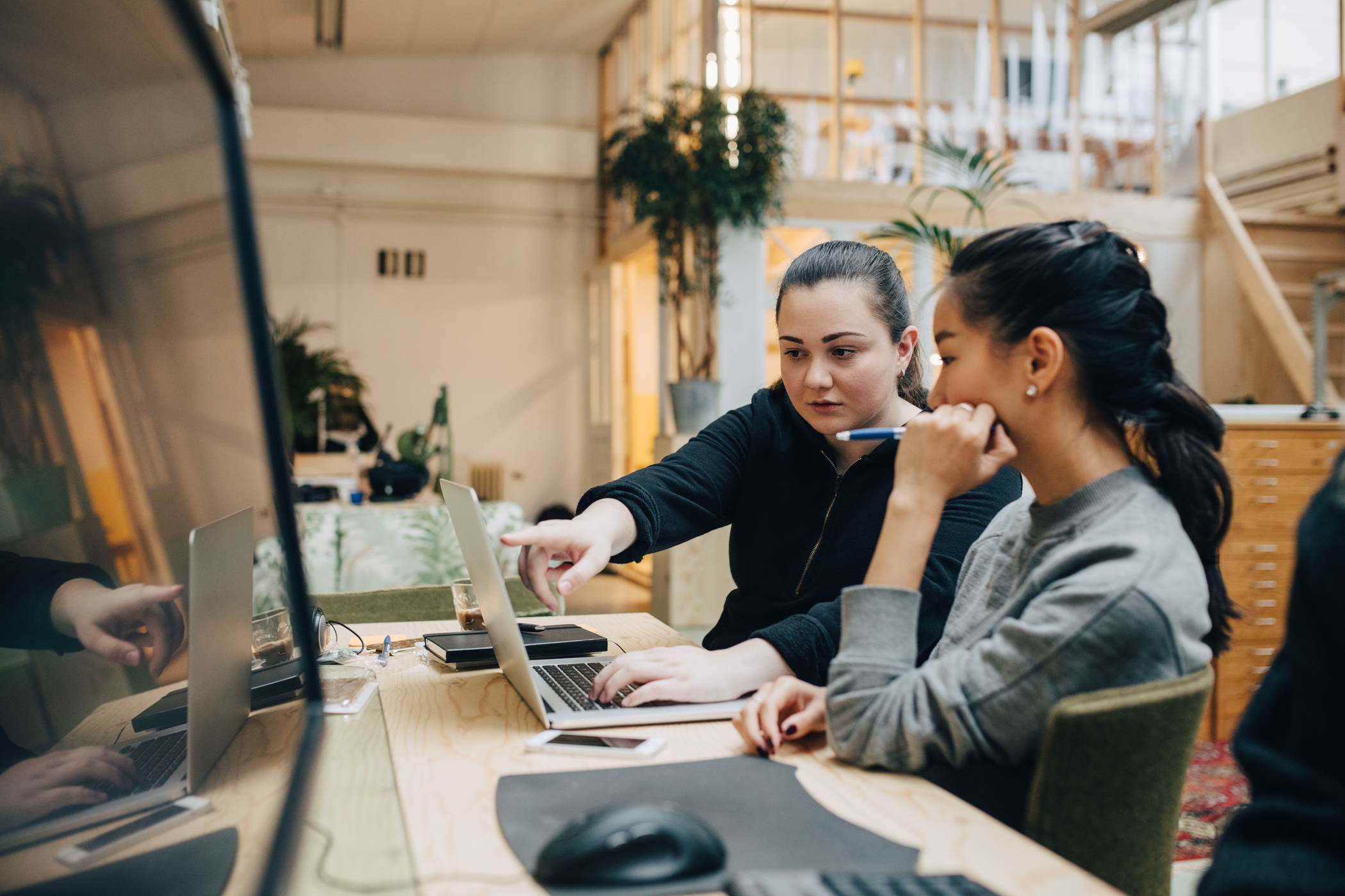 Female coworkers discussing coding on laptop while sitting in office